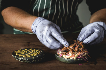 chef in gloves prepares a beef brisket burger close-up on a wooden table