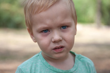 Close up portrait of cute caucasian baby boy with serious expression in blue eyes. Moment of tears. Blonde hair. Outdoors, copy space.