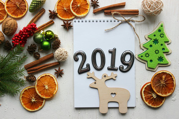 Christmas card, close-up date 2019 on a white paper background surrounded by Christmas balls, fir branches, cinnamon sticks, spices, dried orange, wooden deer . Copy space.