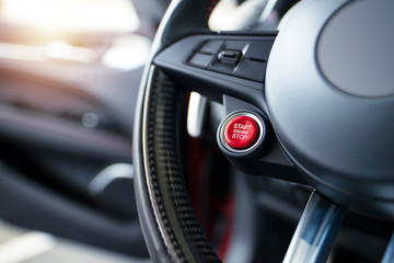Sports car steering wheel with start - stop red button for engine start. Luxury modern car interior.