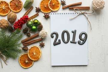 Christmas card, close-up date 2019 on a white paper background surrounded by Christmas balls, fir branches, cinnamon sticks, spices, dried orange, wooden deer . Copy space.