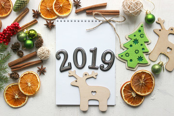 Christmas card, close-up date 2019 on a white paper background surrounded by Christmas balls, fir branches, cinnamon sticks, spices, dried orange, wooden deer . Copy space.