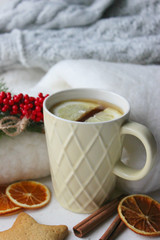 A Cup of tea with lemon on the table close-up surrounded by Christmas decorations and homemade cakes. Star shaped gingerbread, cinnamon sticks and dried oranges on white background.