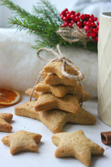 A Cup of tea with lemon on the table close-up surrounded by Christmas decorations and homemade cakes. Star shaped gingerbread, cinnamon sticks and dried oranges on white background.