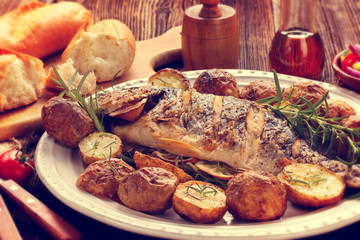 Grilled dorada fish with roasted potatoes and vegetables on the plate