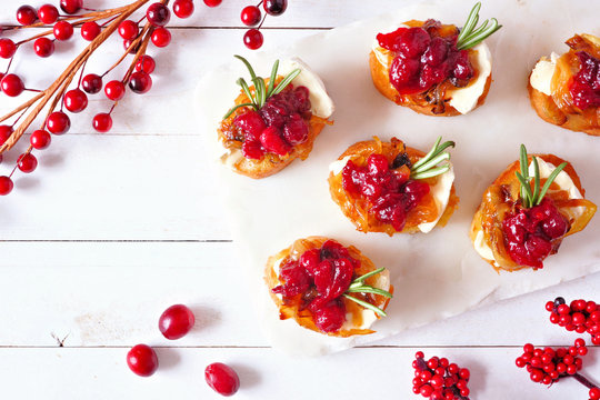 Holiday Crostini Appetizers With Cranberries, Brie And Caramelized Onions. Top View On A White Wood Background.