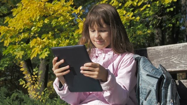 A child with an e-book. A little girl with a tablet in the autumn jacket.