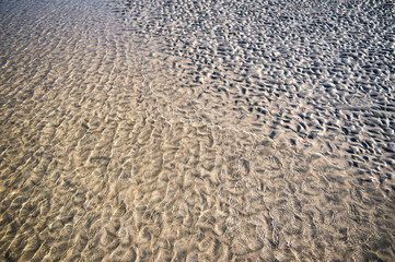 Natural textured background of gentle water washing up on rippled sand on an empty beach