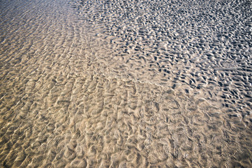 Natural textured background of gentle water washing up on rippled sand on an empty beach