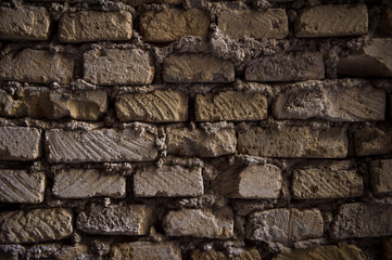 Ancient brick wall background with uneven lines of mortar between shadowy textured old bricks