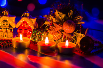 Merry Cristmas. Toy houses and candlelight. Christmas decorations on blurred background. Festive evening. Spruce branches and Christmas toys with bokeh. Copy space