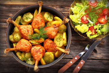 Roasted chicken drumstick with potatoes and salad on wooden background