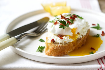 Crispy baguette toasts with cottage cheese, poached egg and dried tomatoes on a light background.
