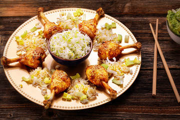 Roasted chicken drumstick with sesame seeds and rice in a plate on a wooden background