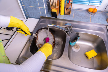 woman with yellow rubber gloves washing dirty pan in the sink