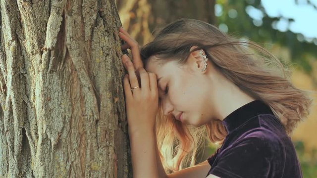 Sad girl leans on a tree in depression.