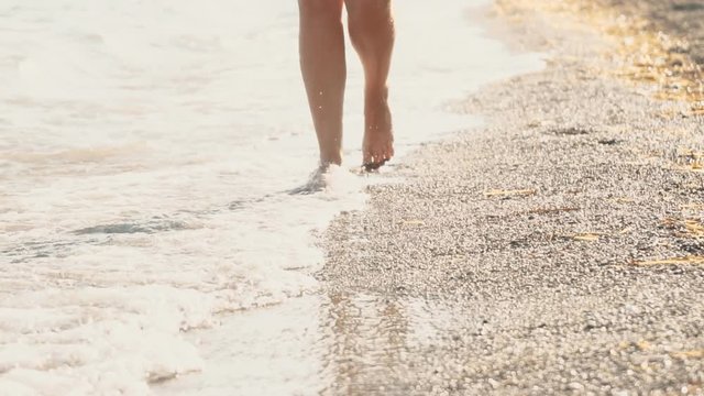 Close-up view of woman's legs walking on the pebble beach.