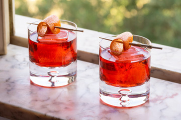 Two Red Negroni Cocktails Drinks on Ice with Orange Twist in Marble Windowsill