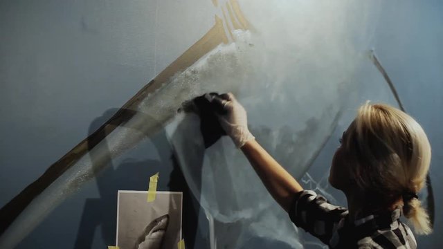 Woman graffiti artist draws a shark on the wall with a sponge and paint