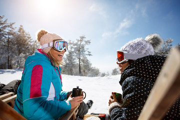 Two female talking with drink in sunbed on ski terrain