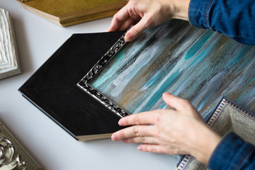 Fototapeta premium Picture framing. Choosing decorative frame for a painting. Woman's hands and samples of frames.