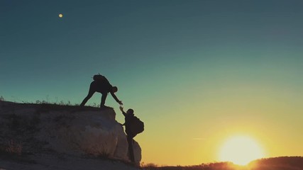 Silhouette of helping hand between two climber. two hikers on top of the mountain, a man helps a man to climb a sheer stone. couple hiking help each other silhouette in mountains with sunlight.