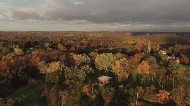 An evening aerial view of the wide colorful Pennsylvania countryside landscape in late Autumn. Power lines and homes in the distance.  	