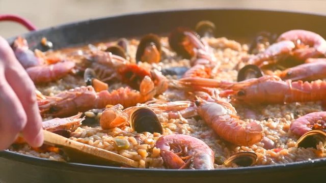 Paella. Person cooking traditional spanish seafood paella with prawns, mussels and fish closeup. Slow motion 4K UHD video footage. 3840X2160