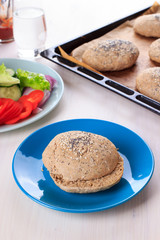 Cooking healthy vegan burger with chickpea fritters, vegetables and whole-wheat bun with sesame and poppy seeds on white table for breakfast