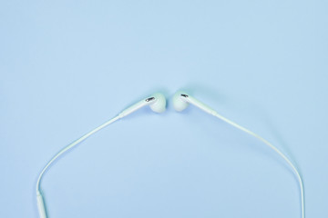 White Earphones or ear buds small talk on sweet blue colour pastel paper, top view, texture and background. music listening concept.