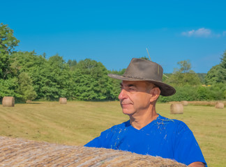 Portrait of a man in a hat behind a haystack in the field..