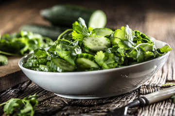 Sliced cucumber on a plate with parsley herb on rustic oak wood.