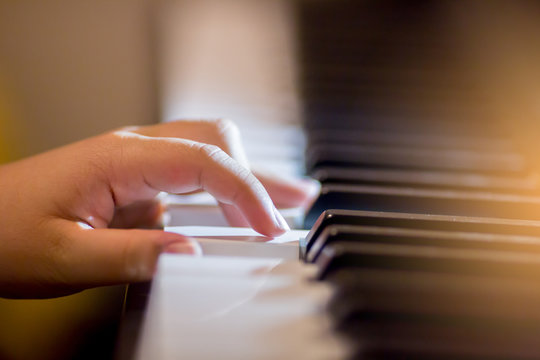 Selective focus of kid fingers and  piano key to play the piano with lighting.