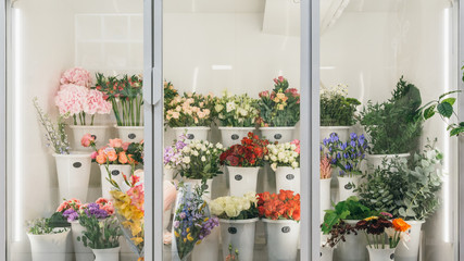 Flower shop concept. Different varieties fresh spring flowers in refrigerator room for flowers. Bouquets on shelf, florist business. - obrazy, fototapety, plakaty