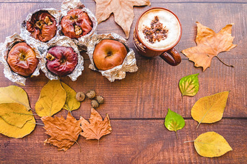 backed apples in foil with cup of coffee and autumn leaves on wooden background