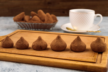Chocolate truffles lined in a row on a wooden Board, a white mug with a saucer for tea.