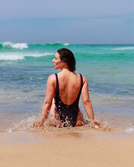 contemplating nature young brunette woman in striking purple swimsuit  at edge of ocean