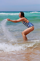 Fototapeta premium Beautiful young woman in swimsuit scooping ocean joy