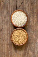 Couscous and sesame seeds in wood bowls on wooden farm kitchen table.