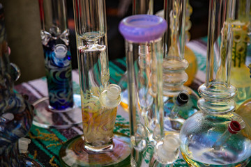 Isolated Close Up View of Glass Bongs on Flea Market Table, Sunlit Out of Focus Background