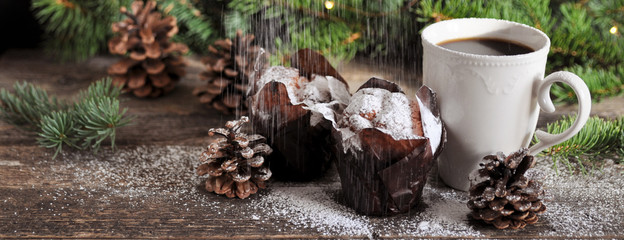 Christmas Breakfast of two cupcakes and a Cup of hot coffee sprinkled with powdered sugar, on the background of fir branches with lights.