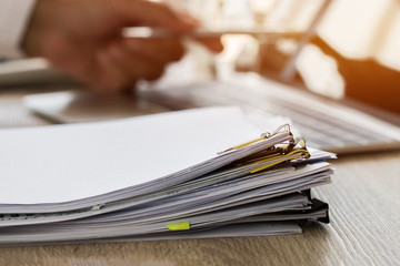Businessman hands holding pen for working in Stacks of paper files searching information business...