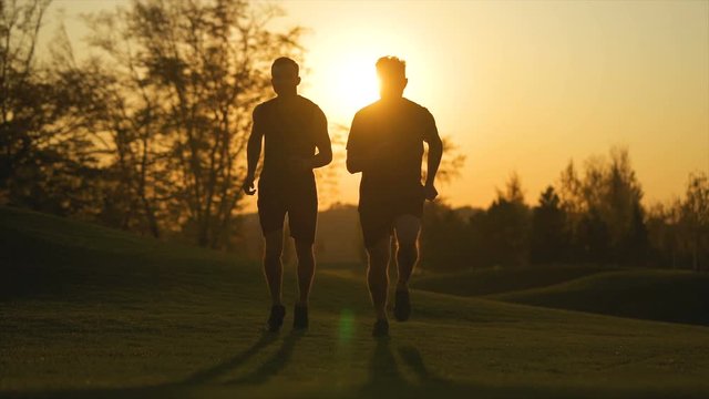 The two men running in the park on the beautiful sunrise background. slow motion