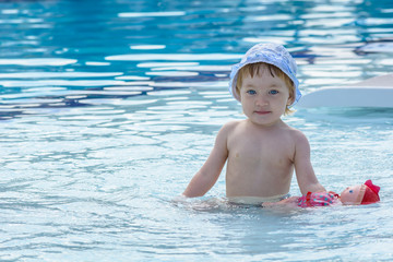 Fototapeta na wymiar Wonderful child in hat plays with doll in blue pool.