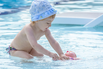 Wonderful child in hat plays with doll in blue pool.