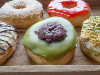 Variety of homemade donuts in wood tray on white background.