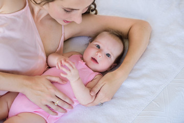 beautiful young mamma cuddling with her 4 months old baby girl on the bed