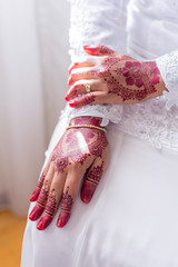 Woman wearing white dress sitting and showing both hands on her lap with henna decoration for...