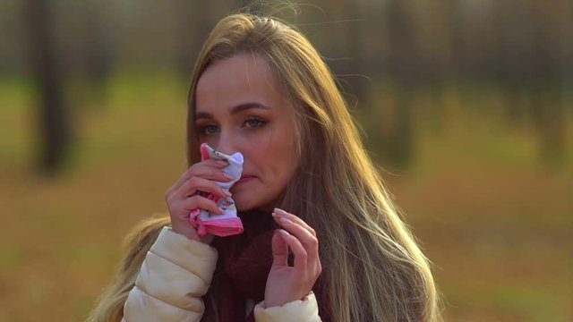 Young attractive girl, caught a cold on the street, wipes her nose with a napkin.