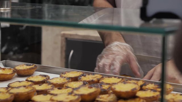 Traditional Portuguese egg hands take tart pasty cakes, dessert Pasteis de nata with different portuguese pastry on the cafe store window, pastel de nata